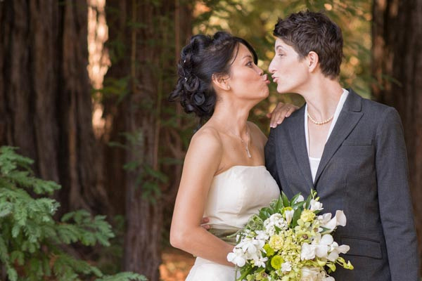 Funny photo of brides kissing with redwoods in background at The Pavilion at Redwood Estates.