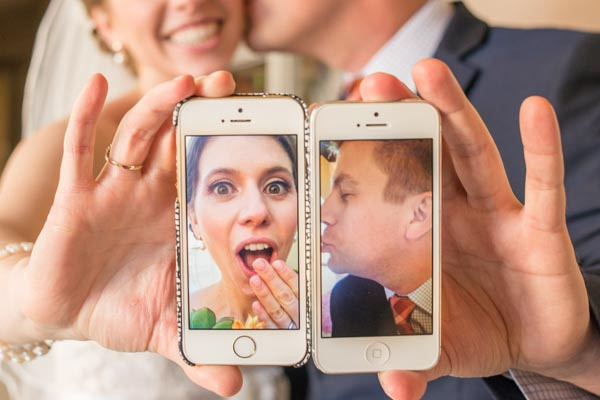 Bride and groom holding two iPhones together with photos from each phone kissing before wedding at Chaminade Resort & Spa.